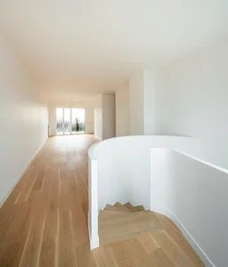 Minimalist modern interior with white walls, wooden stairs, and oak flooring.