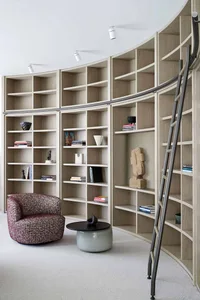 A well-lit, modern library or study space featuring oak shelving units, a comfortable chair, and a ladder for accessing highe