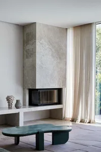 A modern living room featuring a concrete fireplace, light-colored curtains, and a unique green marble coffee table.