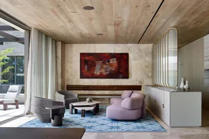 A modern minimalist living room with a lavender sofa, gray chairs, and a blue-patterned rug.