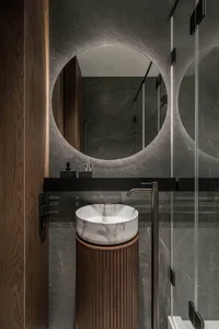 Modern marble bathroom with circular mirror and sink on wooden pedestal.