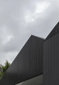 Modern building with dark, metal-clad exterior under a cloudy sky.