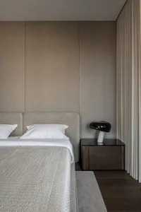 A modern minimalist bedroom with a neutral color palette, featuring a sleek upholstered bed, a dark wood bedside table with a