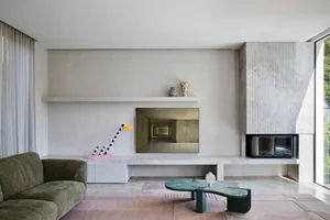 A minimalist living room with a concrete fireplace, large windows, and a simple sofa.