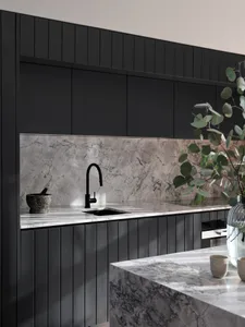 Modern minimalist residential kitchen featuring marble countertops, black steel accents, and concrete flooring.