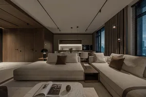 A modern minimalist living room featuring a woven sofa with cushions, a coffee table, and an open-plan kitchen area with a di