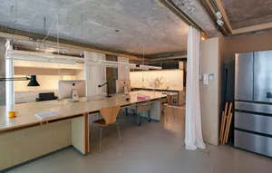 A modern office space featuring a concrete ceiling, wooden furniture, and stainless steel appliances.