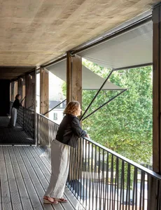 A modern residential balcony featuring wood and metal structures, overlooking greenery.