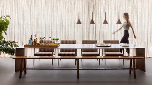 A contemporary restaurant dining room featuring wooden furniture, upholstered seats, and glass pendant lights.