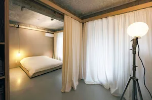A minimalist bedroom with textured concrete floors and white curtains.
