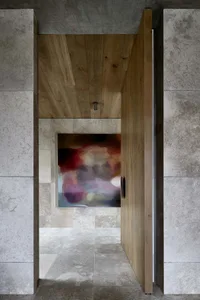An open-plan minimalist interior design featuring a wooden door with a colorful abstract mural and textured concrete walls.