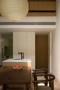 A minimalist residential kitchen featuring a modern wooden table, white cabinetry, and a large spherical light fixture.