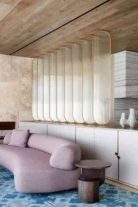 A modern living room with a curved, lilac-colored sofa, a wooden coffee table, a blue and white patterned rug, and a glass sc