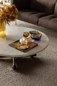 A stylish modern living room featuring a marble coffee table adorned with glass decorative items and a bouquet of flowers.
