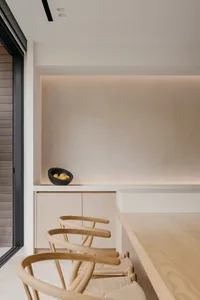 A modern minimalist kitchen with wooden elements features a sleek, white countertop, wooden chairs, and a black bowl filled w