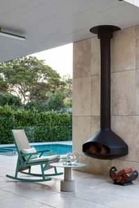A contemporary outdoor lounge area featuring a minimalist metal fireplace, a rocking chair, a small coffee table, and a glass