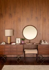 A modern vanity station with a round mirror, a lamp, and various items on a wooden surface.