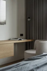 Open book on a modern minimalist bedside table with a wooden desk and upholstered chair.