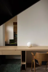 Modern home office featuring a minimalist wooden desk with a white spherical object and a retro green chair, against white wa