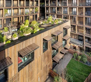 An aerial view of modern wooden apartments with a rooftop garden featuring various plants and trees.