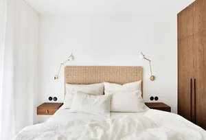 Minimalist bedroom featuring a woven headboard, white linen bedding, and wooden nightstands with wall-mounted lamps.