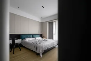 A modern minimalist bedroom featuring a sleek, white bed with a blue leather headboard, paired with a white dresser and woode