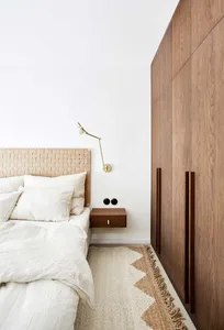 A minimalist, modern bedroom with a wood headboard and linen bedding.