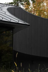 Modern building with black metal exterior and curved roof against a backdrop of autumn trees.