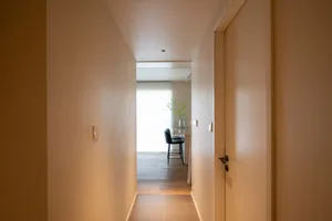 A modern corridor featuring minimalist concrete tiles on the floor, leading towards a dining area with a black chair and flor
