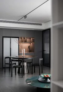 A modern dining room features a metallic table with dark chairs, illuminated by sleek lighting and surrounded by minimalist b