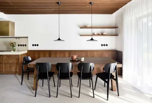 A modern dining room featuring a wooden table and chairs, with a white curtain and floating shelves.