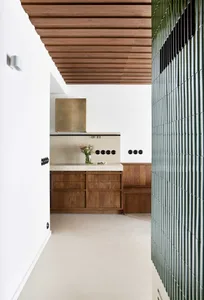 A modern kitchen interior with marble countertops, concrete backsplash, and wooden cabinets.