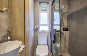 A modern minimalist bathroom with white oval sink, white toilet, and ceramic tiles. Features include a window, glass shower e