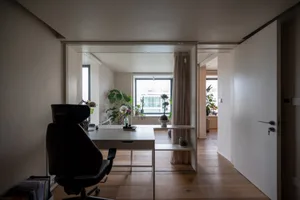 A minimalist home office with a white desk and chair, surrounded by plants and natural light.