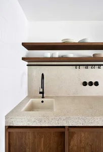 Modern minimalist kitchen with concrete countertops, white backsplash, and wooden shelves.