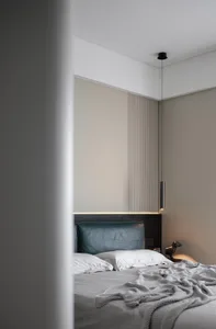 A modern bedroom with a blue velvet headboard, white bedding, and a metal pendant light.
