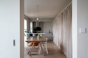 A modern minimalist kitchen with a wooden table, fabric curtains, and metal chairs.
