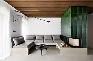 A modern living room with a green feature wall made of bamboo panels, a concrete floor, and a grey sectional sofa.