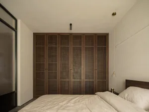 A minimalist bedroom featuring wooden paneled storage cabinets, a bed with a beige comforter, and a hanging lamp.