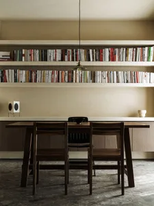 A minimalist dining room featuring a wooden table, chairs, and built-in bookshelves.