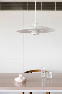 A minimalist interior space featuring a white table with a wooden texture, a white pendant light fixture, and glass cups.