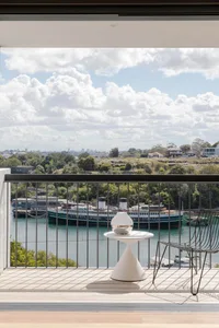 A modern balcony featuring a metal table and chair, with a scenic river view and ships in the background.