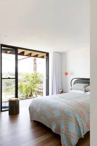 A modern bedroom featuring wooden flooring and a bed with a blue and beige patterned blanket.