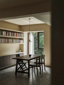 Modern industrial home office with wooden table, concrete floor, and bookshelves filled with books.