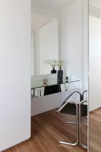 A modern minimalist bathroom featuring a glass countertop, white walls, and wooden flooring.