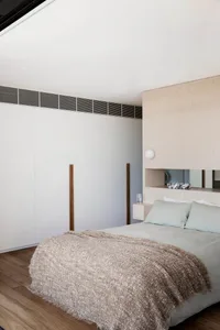 Modern minimalist bedroom featuring a bed with a wooden headboard and decorative wood panels, topped with a plush throw blank
