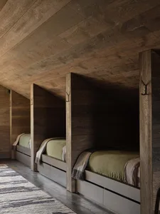 A minimalist bedroom featuring wooden walls and floors, with three single beds in a slanted room.