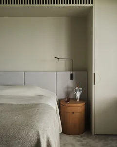 A minimalist bedroom with a grey upholstered bed, wooden nightstand, and sleek black swing arm lamp.