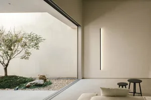 A minimalist hotel room with concrete and wooden elements, featuring a large window and a small rock garden with a small tree