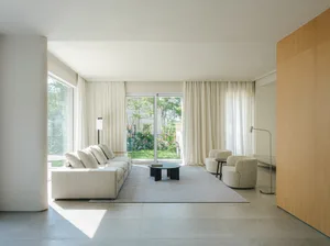 A minimalist living room featuring a white sectional sofa, a small round table, and a modern floor lamp with a white curtain 